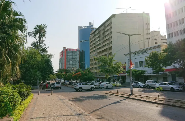 Traffic and office blocks along Avenida Samora Machel in central Maputo, palms and flame trees lining the pavement.