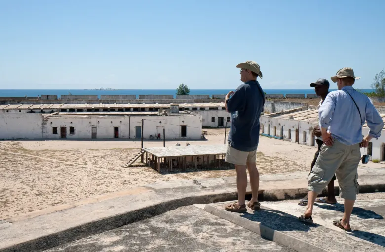 Visitors standing on the ramparts of São Sebastião Fortress looking down into its courtyard, the sea beyond.