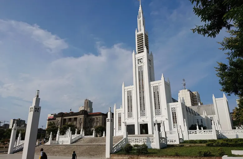The white Art Deco cathedral in Maputo with the city hall and apartment blocks behind it under a blue sky.