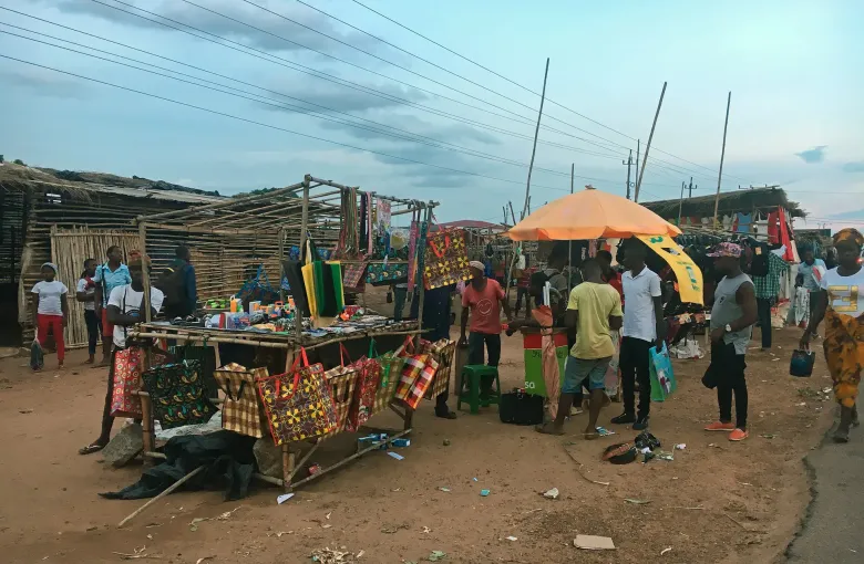 Roadside stalls in Nampula hung with printed bags and household goods under an orange umbrella at dusk.