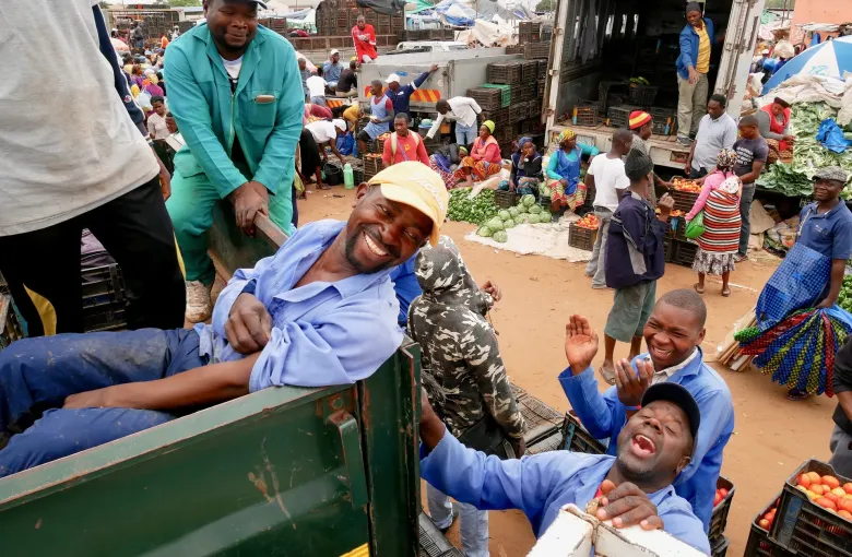 Traders loading crates of produce at Zimpeto market in Maputo, with cabbages and tomatoes laid out on the ground behind.