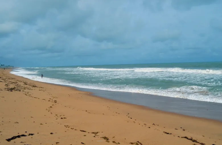 Surf breaking on the wide empty Atlantic beach at Badagry, Lagos State, Nigeria, under a heavy overcast sky.
