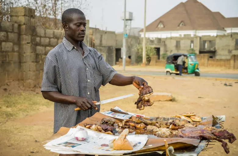 A vendor slicing suya from skewers at a roadside stall in the Asokoro district of Abuja, Nigeria.