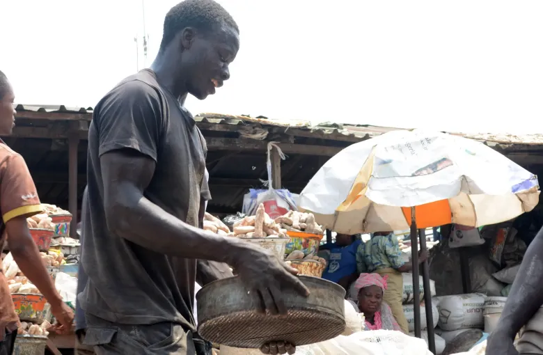 A trader weighing produce in a basket at a stall under umbrellas at Mile 12 market in Lagos, Nigeria.